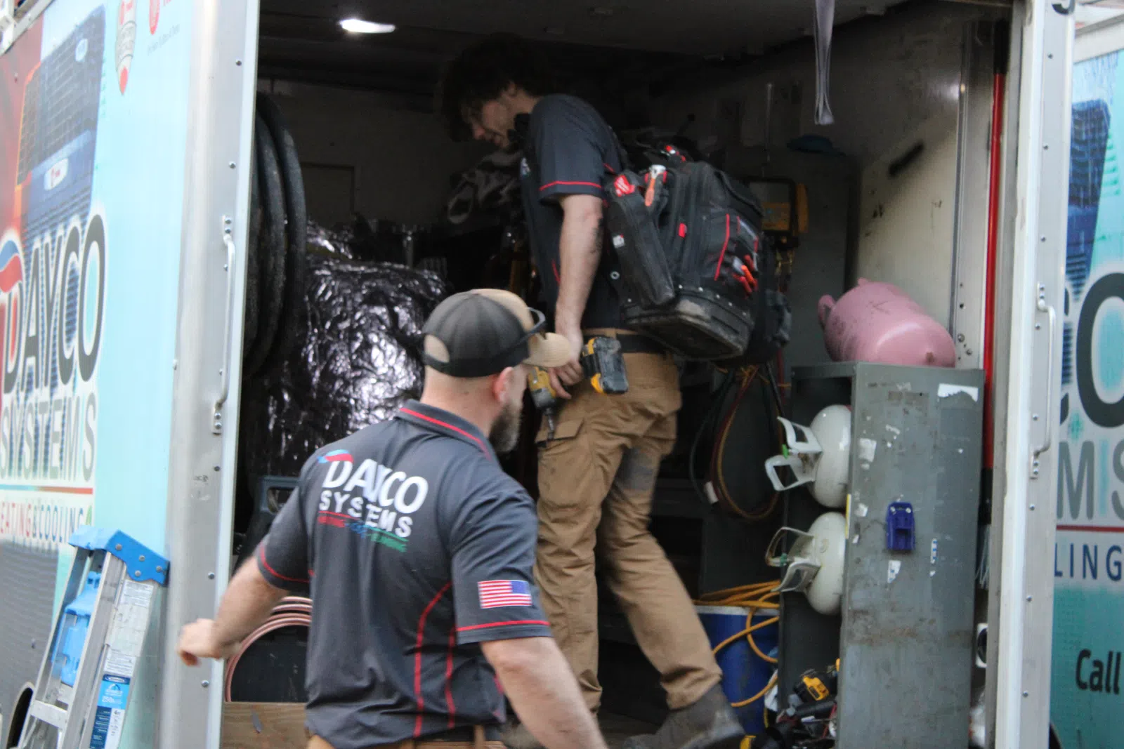 Two technicians with DAYCO Systems uniforms working inside a service truck filled with tools and equipment.