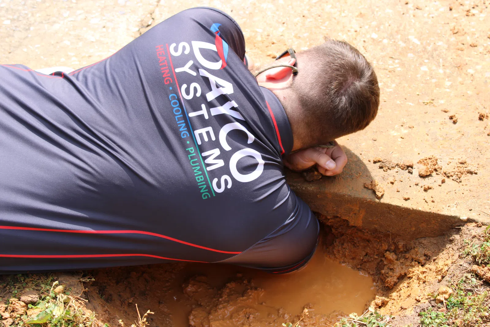 Technician from Dayco Systems inspecting a muddy outdoor plumbing or drainage site laying on the ground.