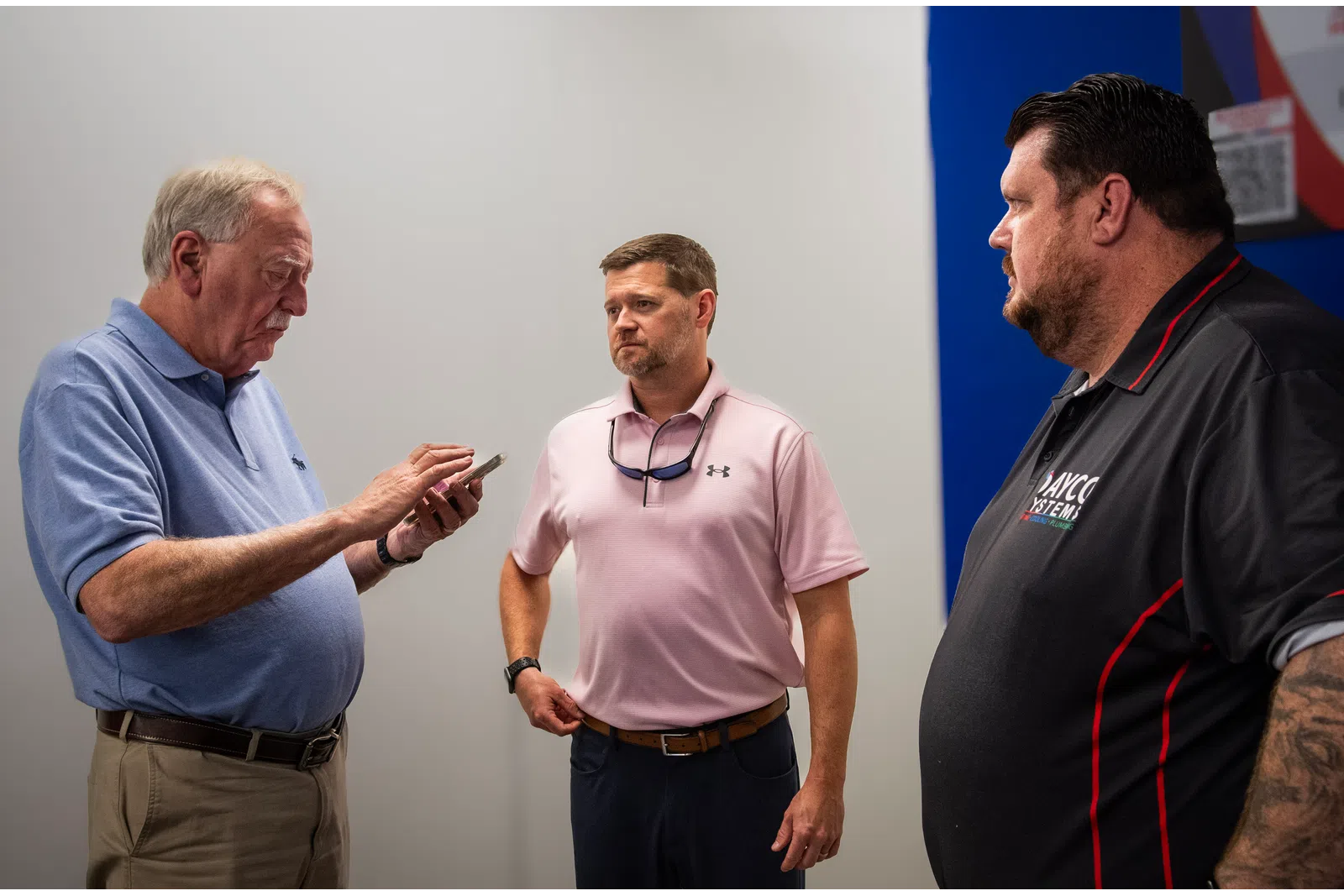 Three men having a serious conversation indoors, one using a smartphone, others listening attentively.