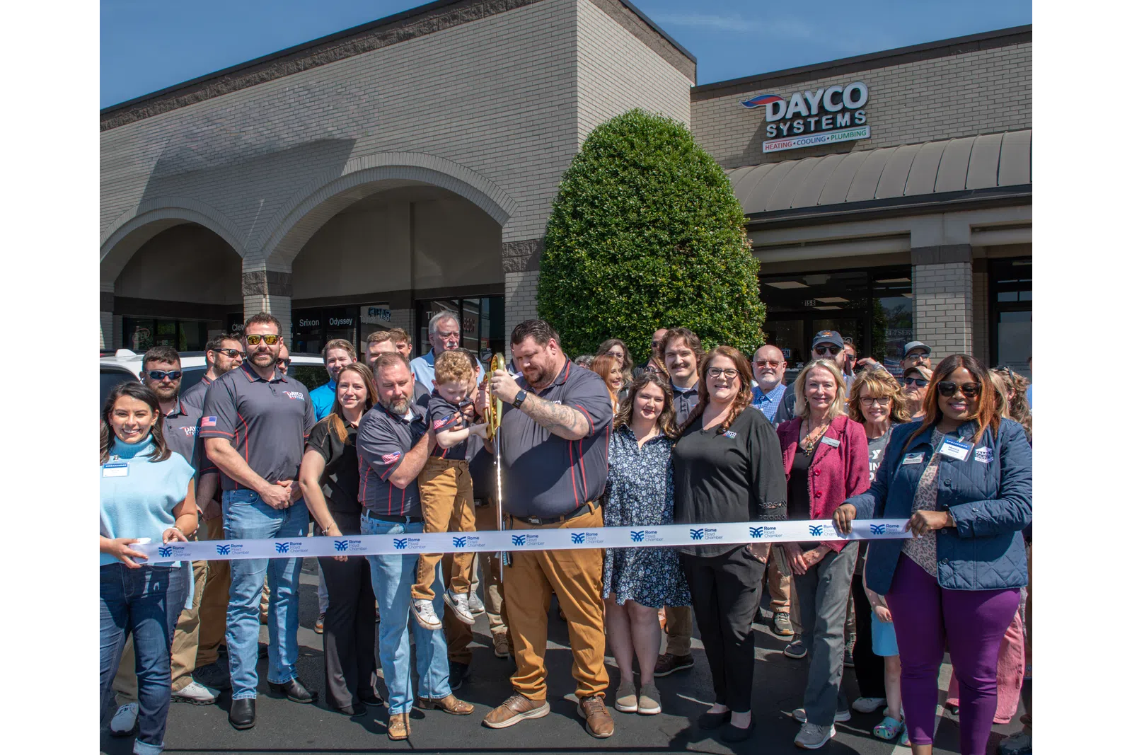 Group of people at a ribbon-cutting ceremony outside Dayco Systems building on a sunny day.