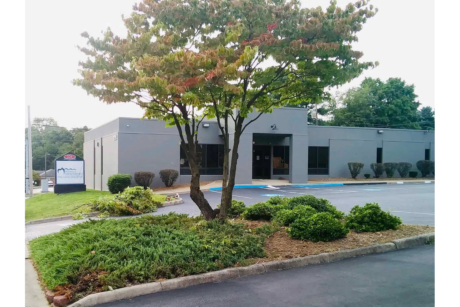 Gray office building with landscaped greenery and parking lot under a partly cloudy sky.