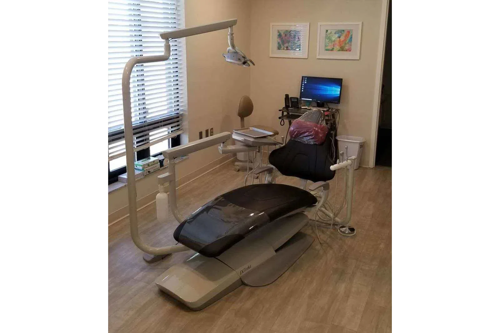 Modern dental clinic room with a reclining patient chair, overhead light, computer, and medical equipment.
