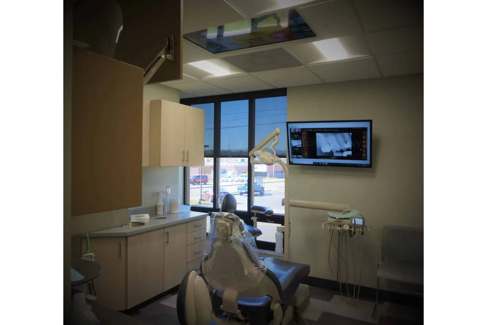 Modern dental office with exam chair, dental equipment, cabinets, and X-ray displayed on wall-mounted screen.