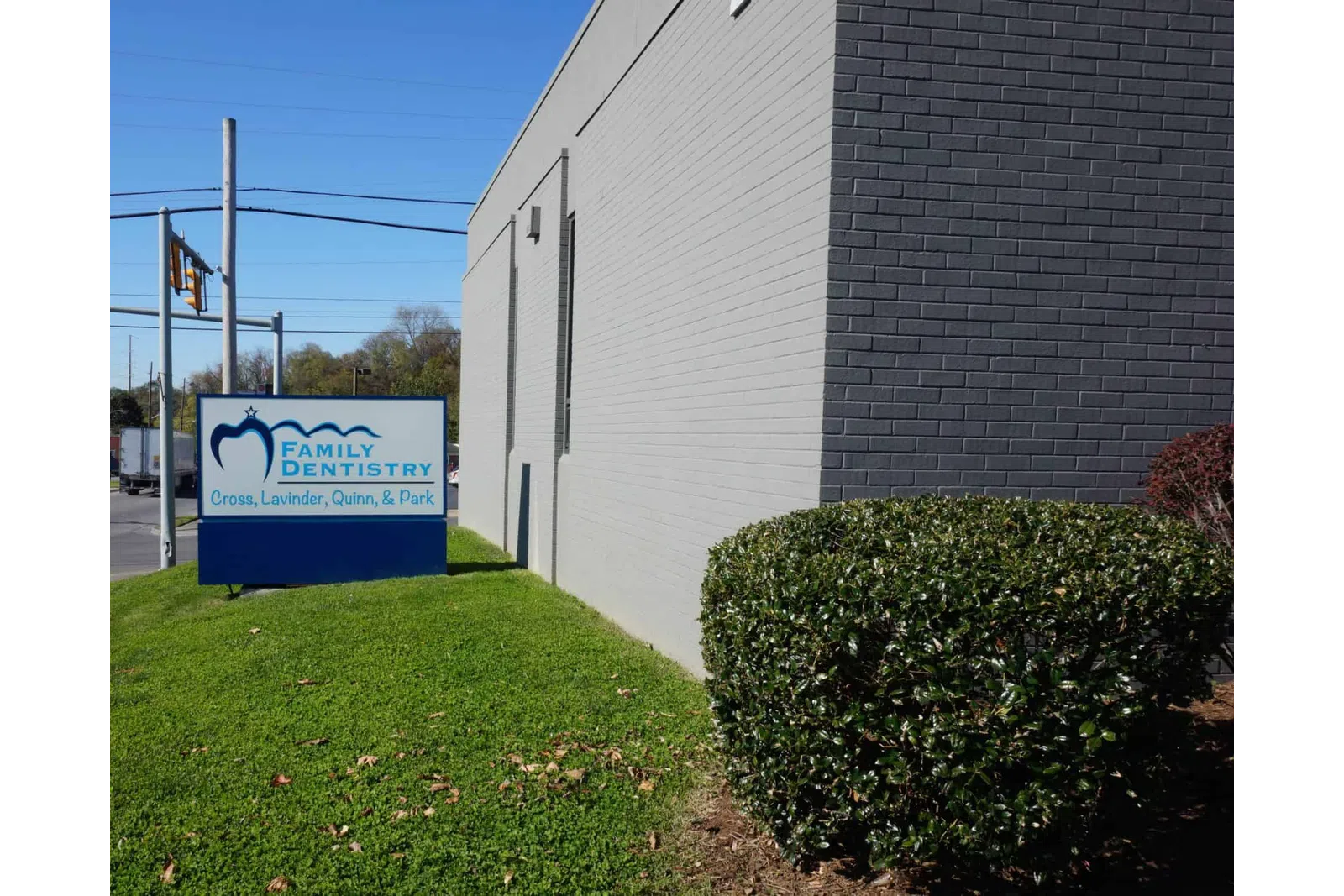 Family Dentistry sign near gray brick building with green lawn and bush under clear blue sky.