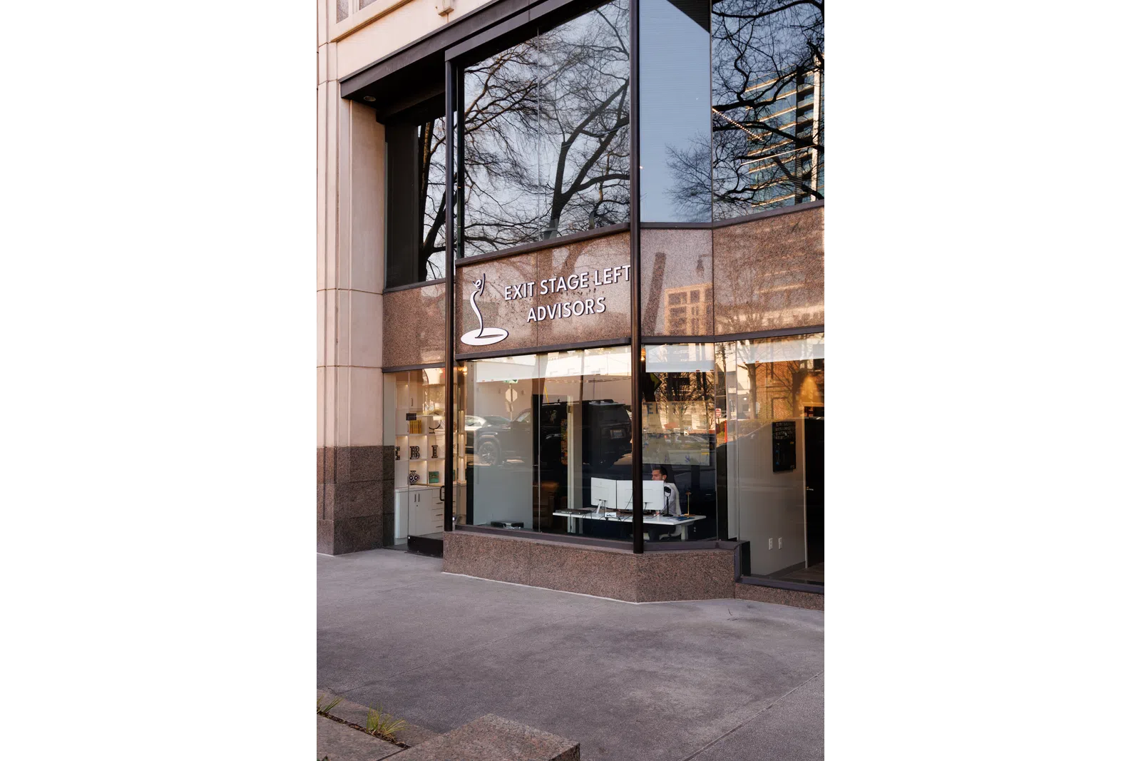 Modern office building exterior with large glass windows and EXIT STAGE LEFT ADVISORS sign.