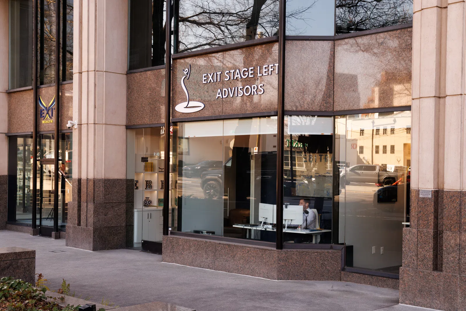Office building exterior with large windows showing Exit Stage Left Advisors signage and a person working inside.