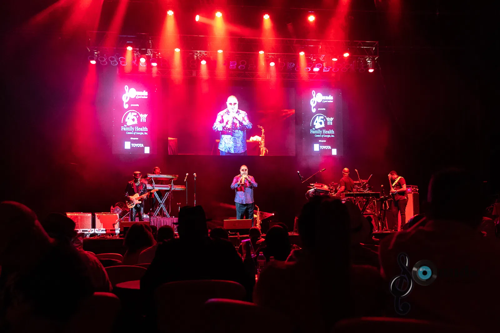 a group of people sitting on stage with stage lights and an audience