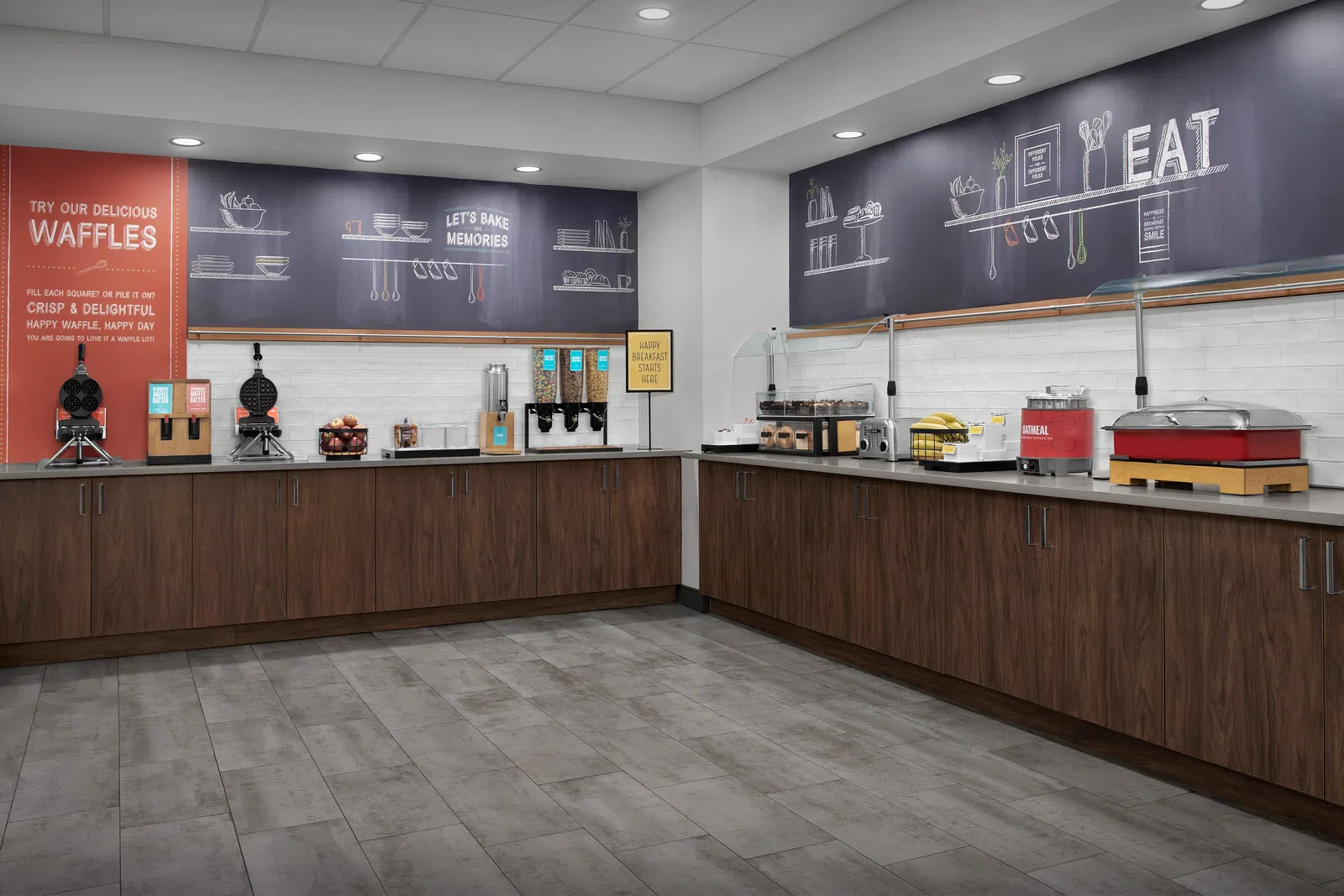 Modern breakfast buffet area with waffle makers, cereal dispensers, and wooden cabinets in a clean, spacious room.