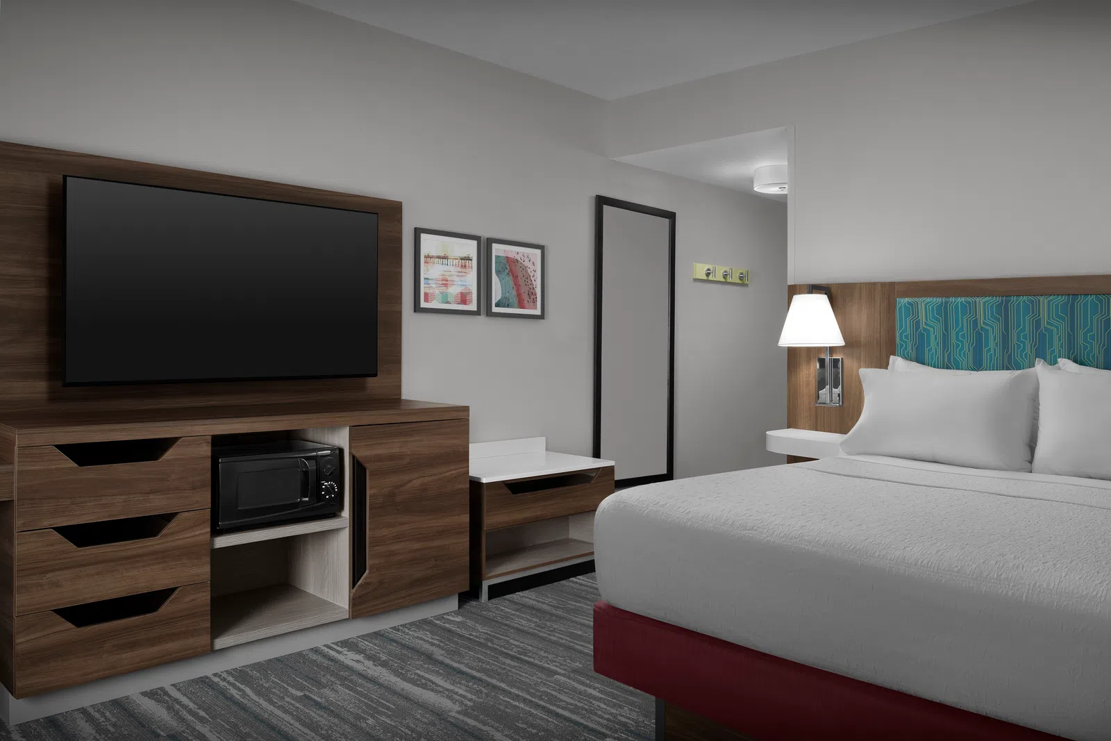 Modern hotel room with a large bed, wall-mounted TV, wooden furniture, microwave, and framed artwork on the wall.