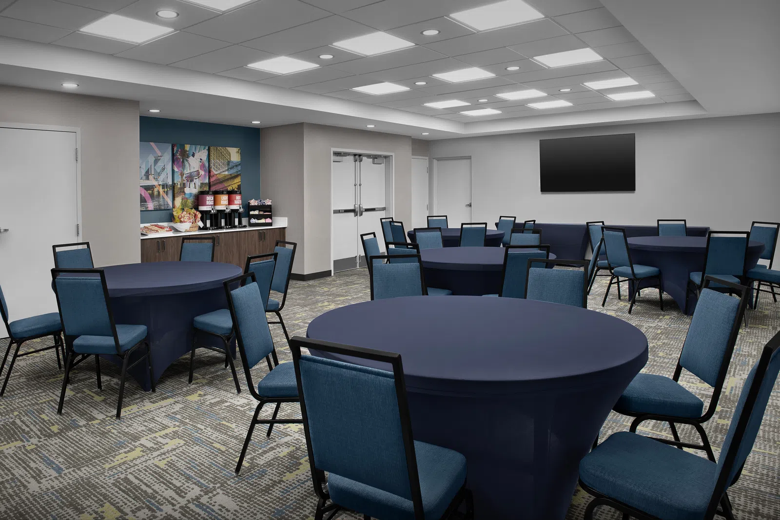 Modern conference room with round tables covered in dark cloths and blue chairs under bright ceiling lights