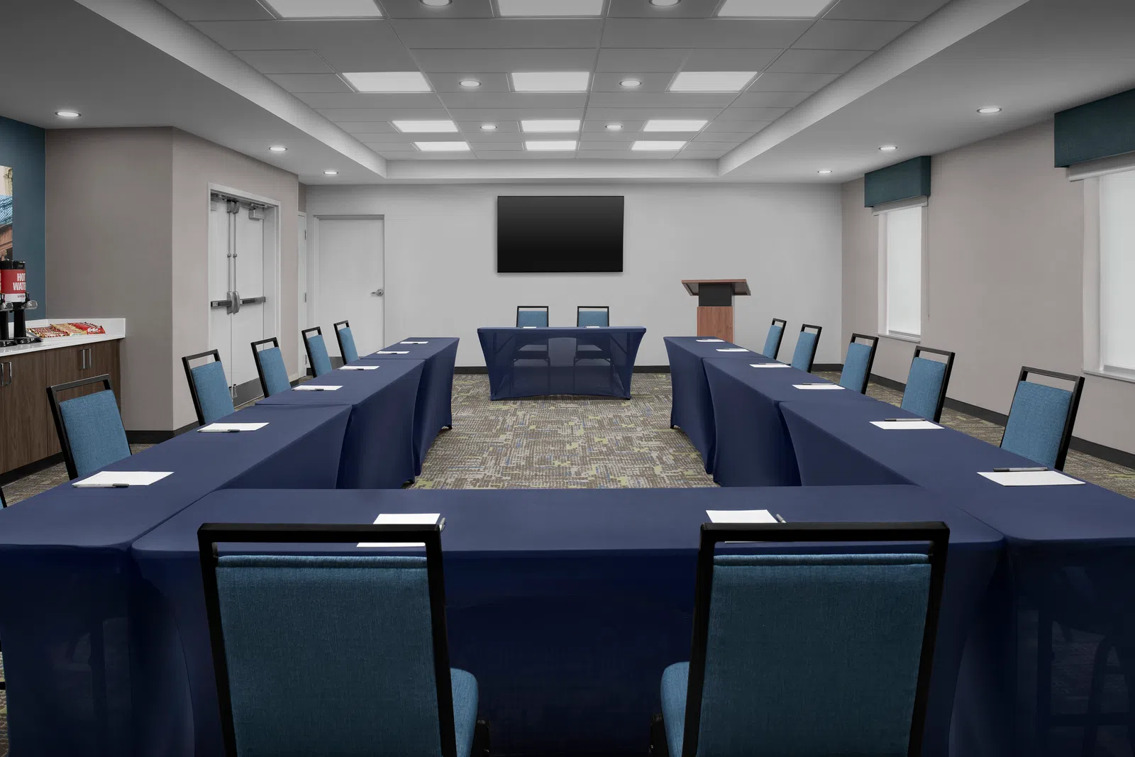 Modern U-shaped conference room with navy table covers, blue chairs, podium, and large screen on white wall.