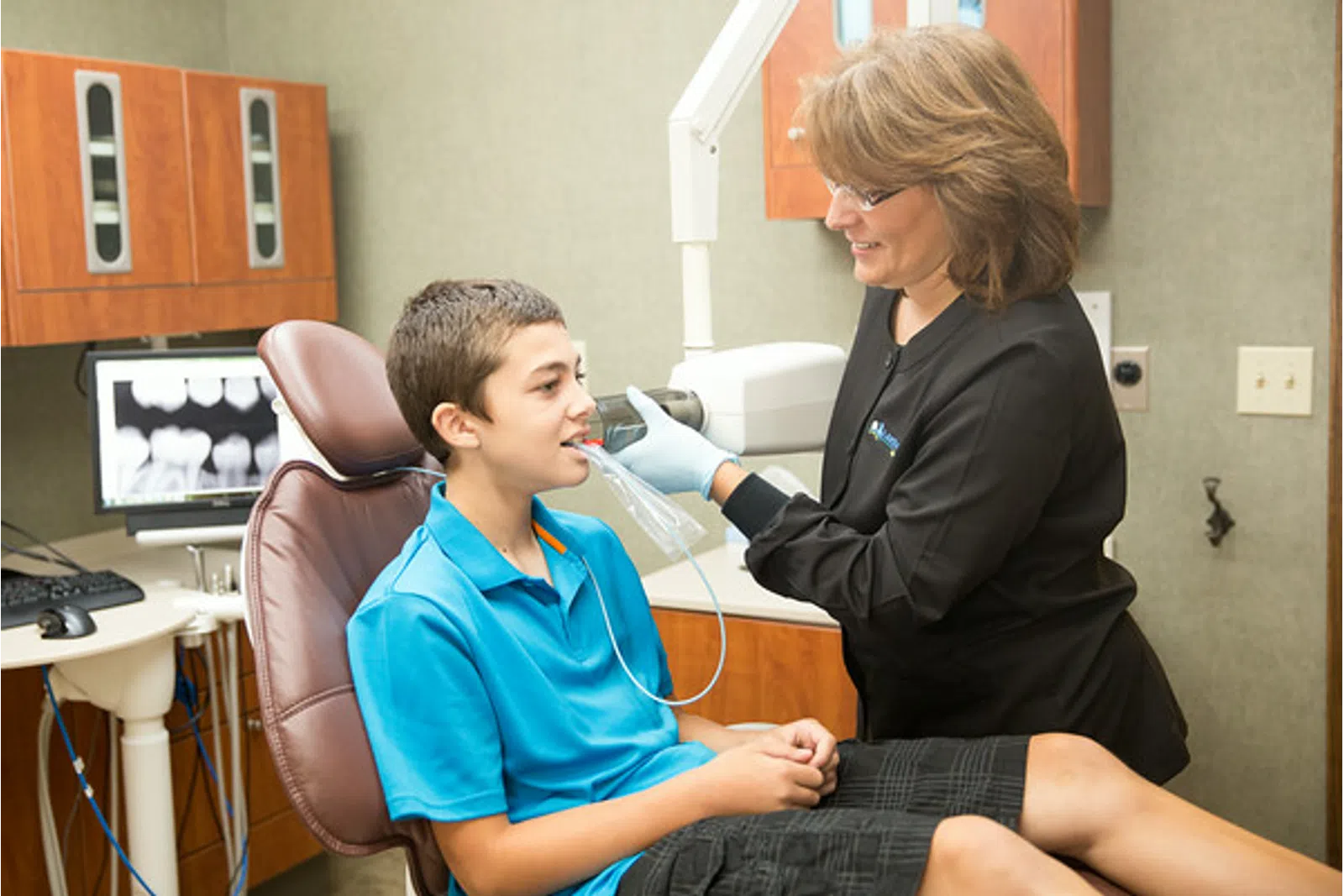 Dentist fitting a young boy with a dental mouthpiece in a modern dental office with x-ray monitor
