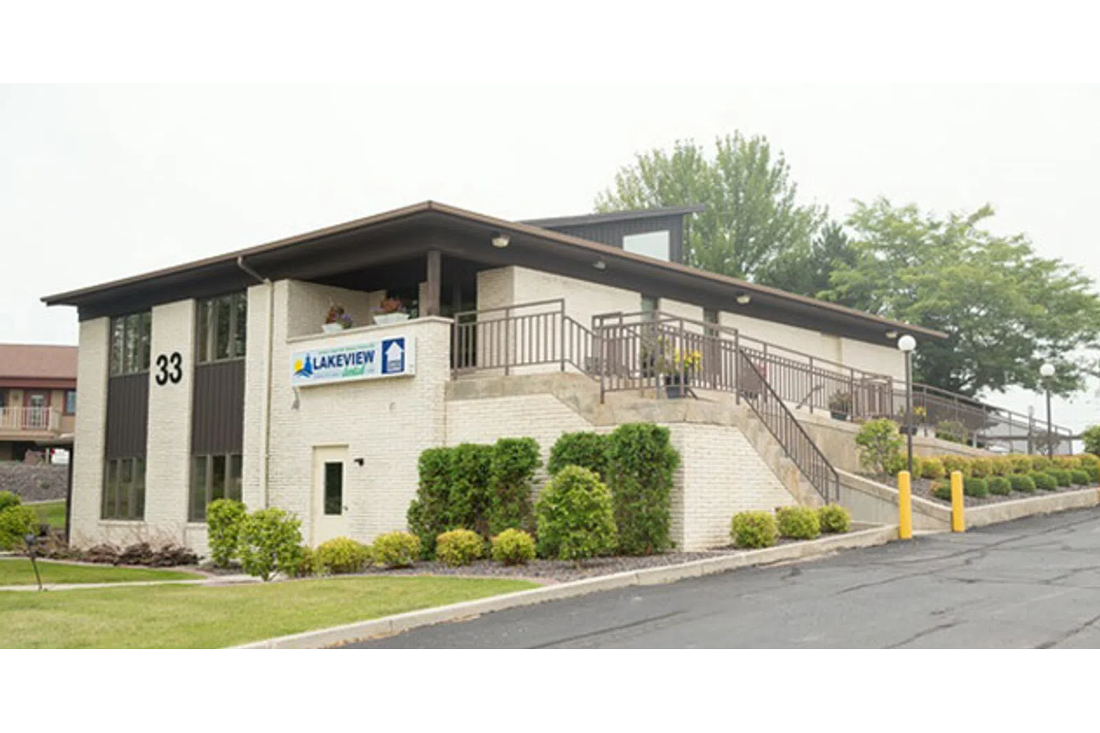 Modern two-story Lakeview building with stairs, railings, greenery, and a parking lot under an overcast sky