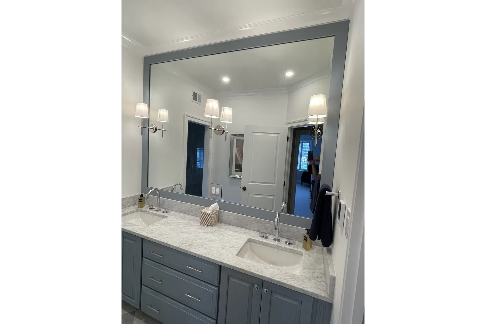 Modern bathroom vanity with double sinks, marble countertop, large gray framed mirror, and wall-mounted lights.
