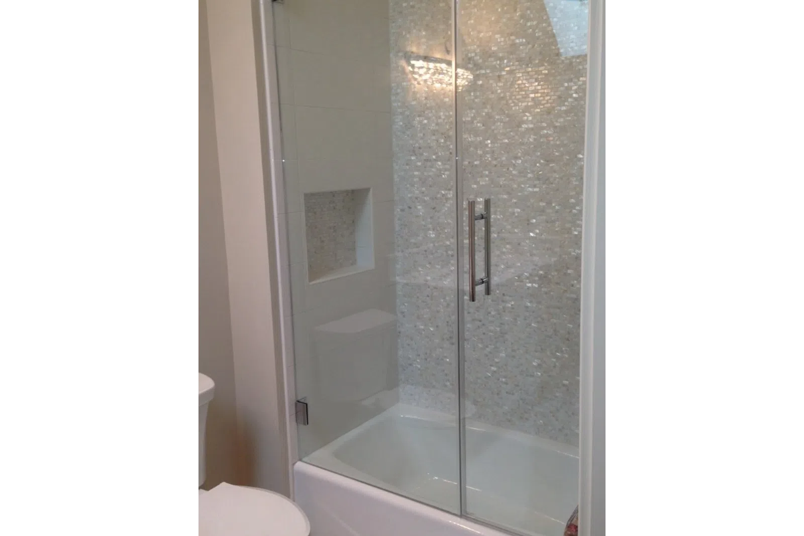 Modern bathroom shower with glass sliding doors and mosaic tile wall inside the tub area.