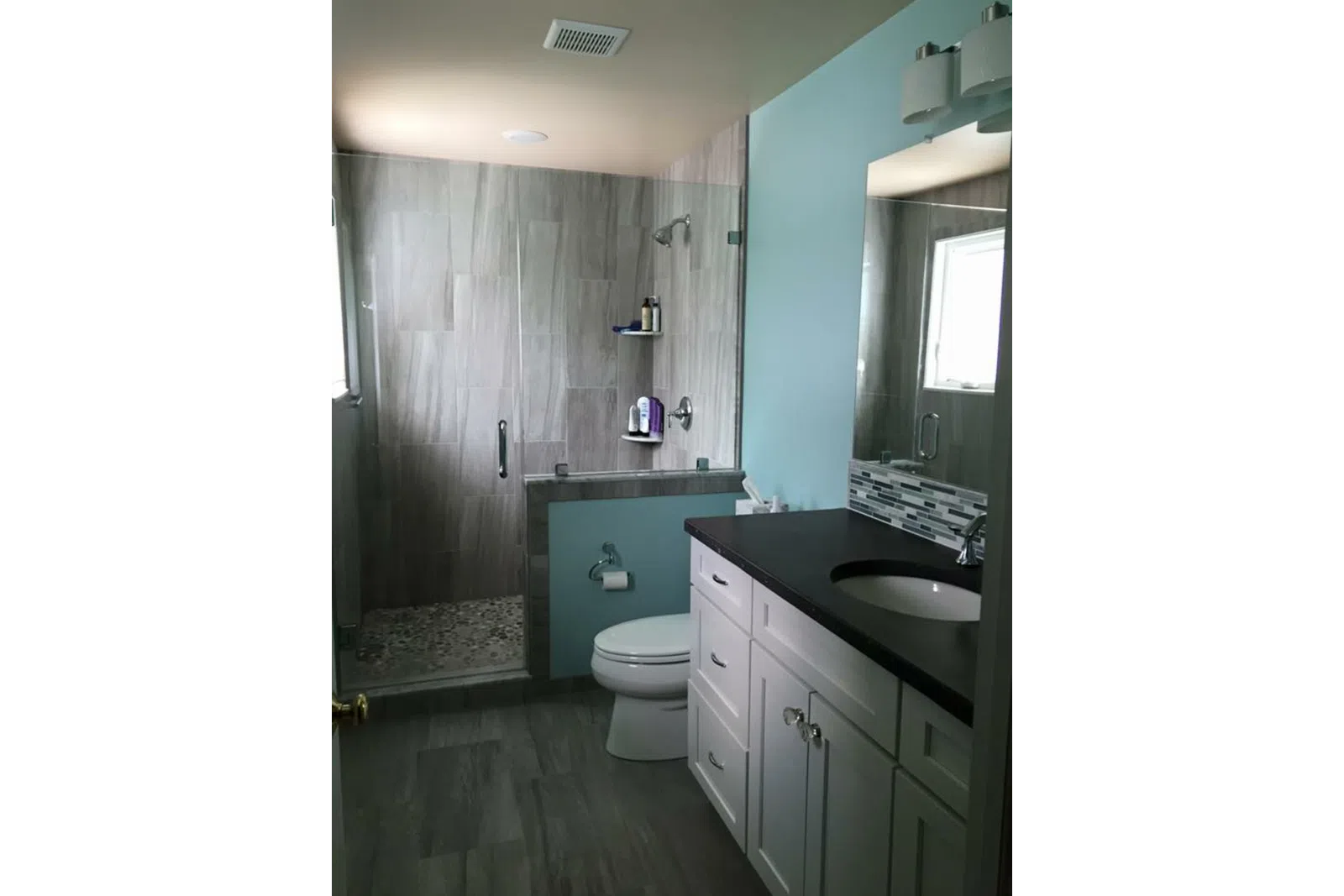 Modern bathroom with glass shower, light blue walls, white vanity, and dark countertop with large mirror.