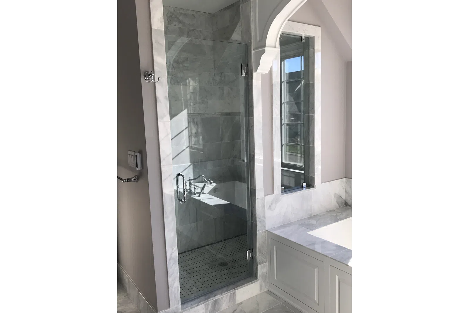 Modern bathroom with glass shower enclosure, marble tiles, built-in bathtub, and large window.