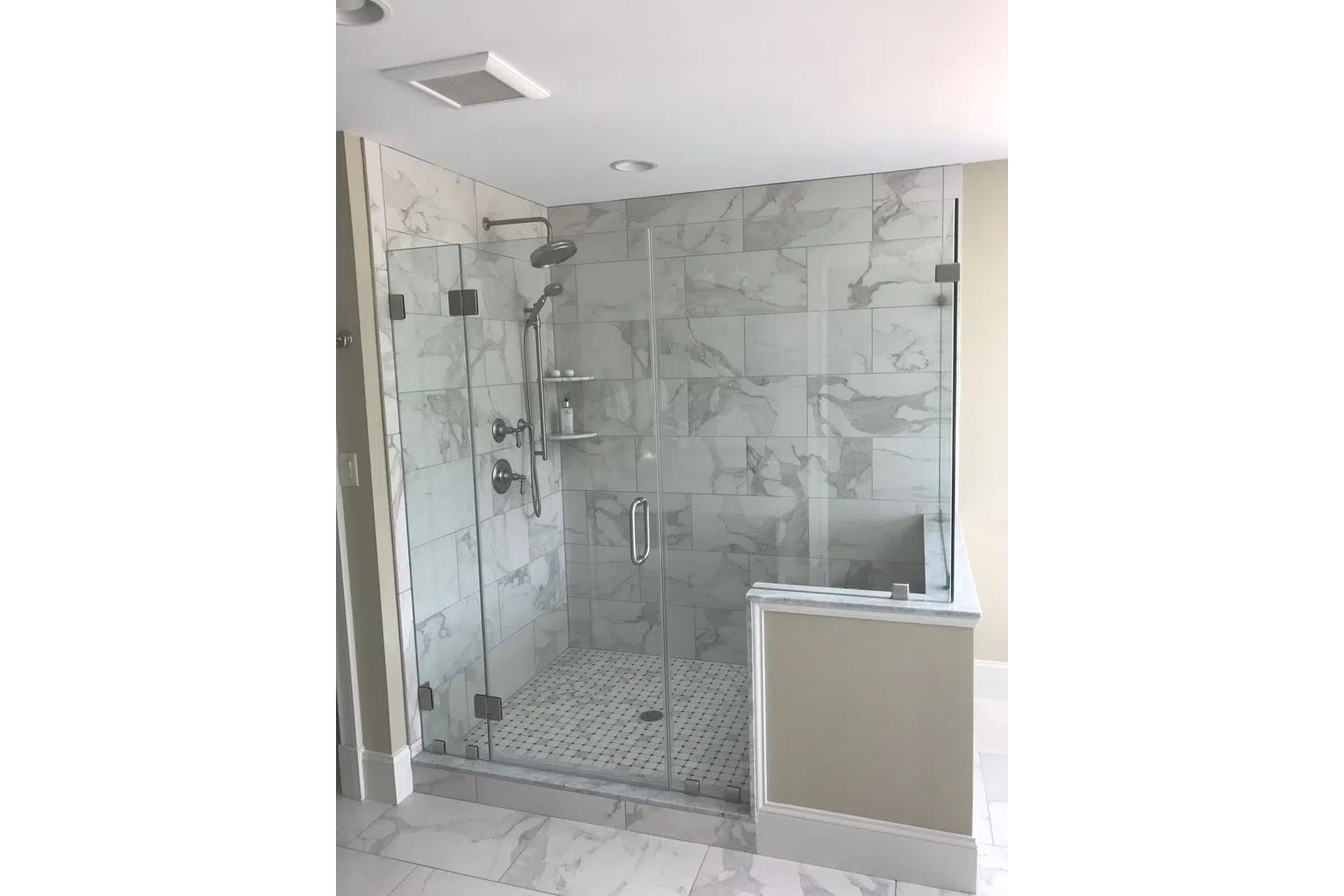 Modern glass-enclosed walk-in shower with marble tiles and rain showerhead in a bright bathroom.