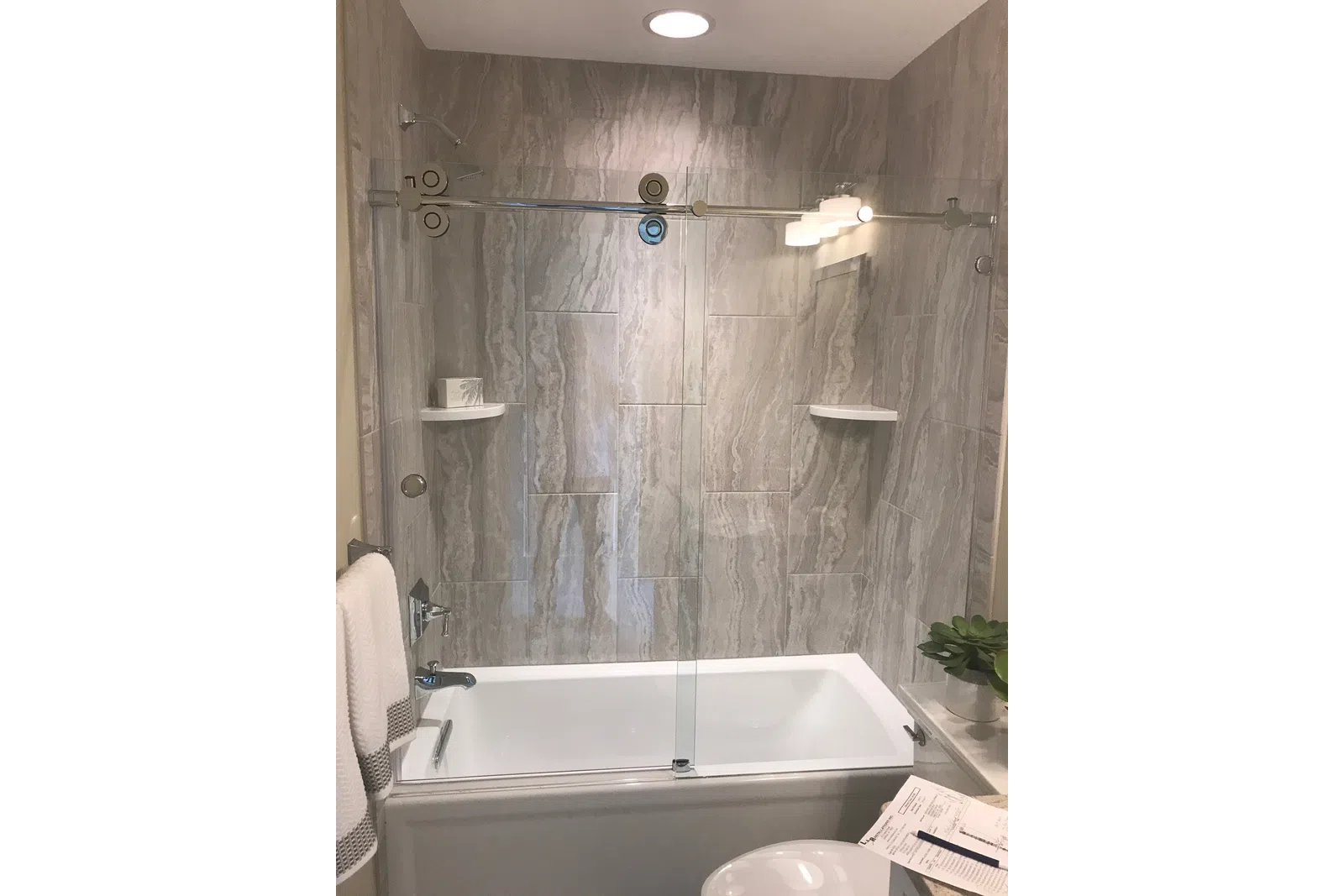 Modern bathroom with a white bathtub, glass sliding door, marble wall tiles, and towels on a rack.