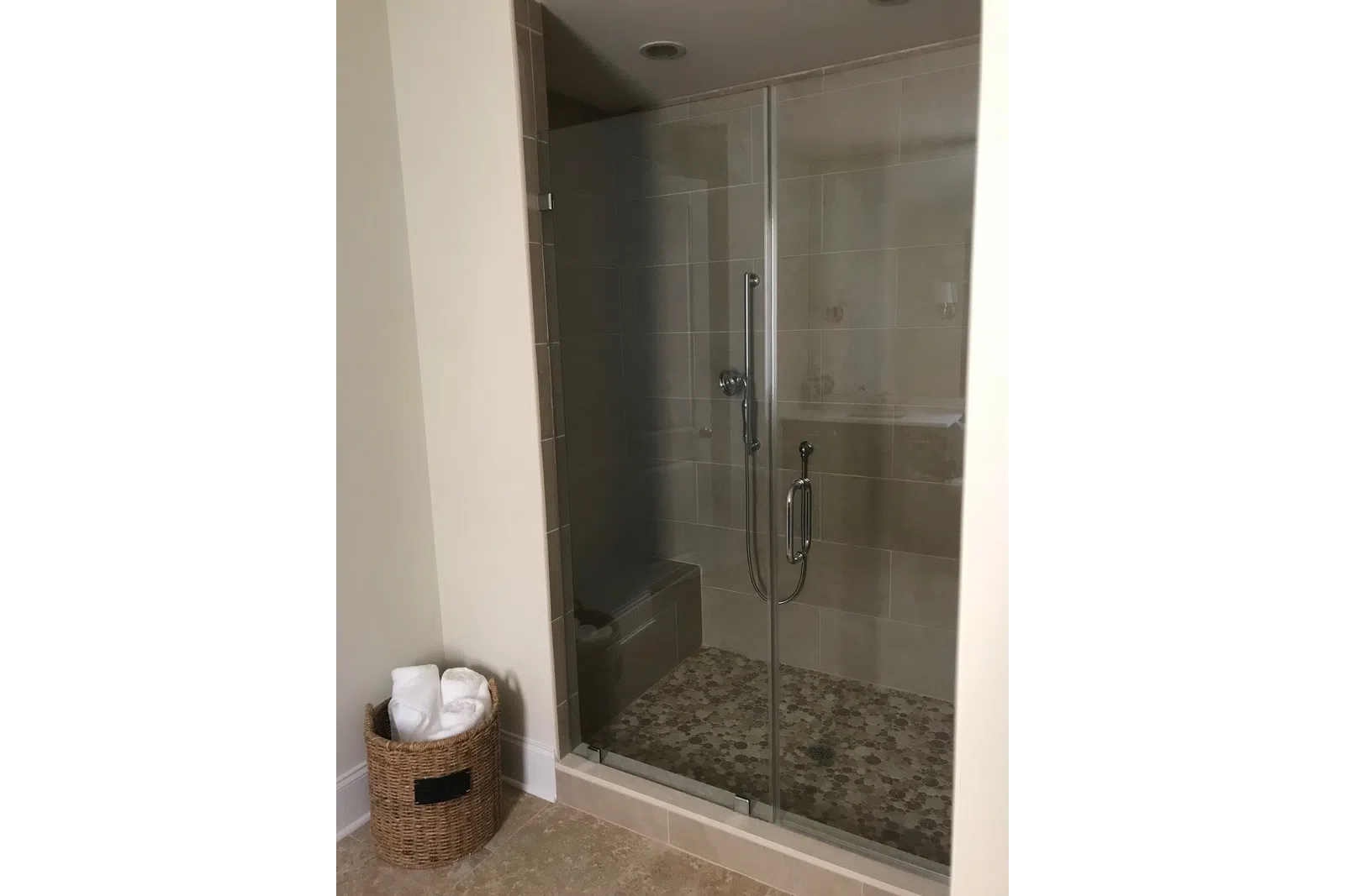 Modern tiled walk-in shower with glass doors, built-in bench, and a wicker basket with white towels nearby.