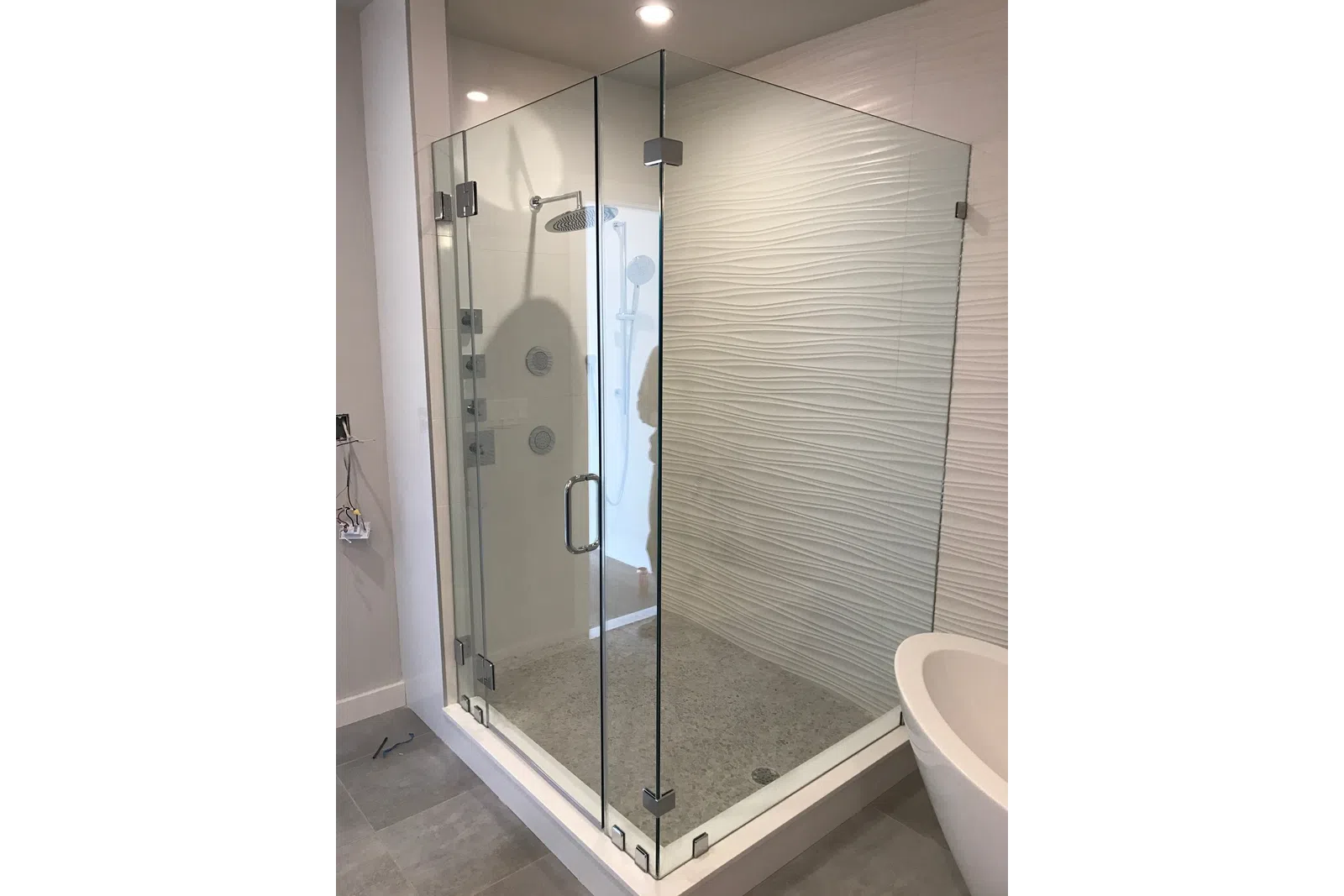 Modern bathroom with glass shower enclosure, textured wall tiles, rain showerhead, and freestanding bathtub.