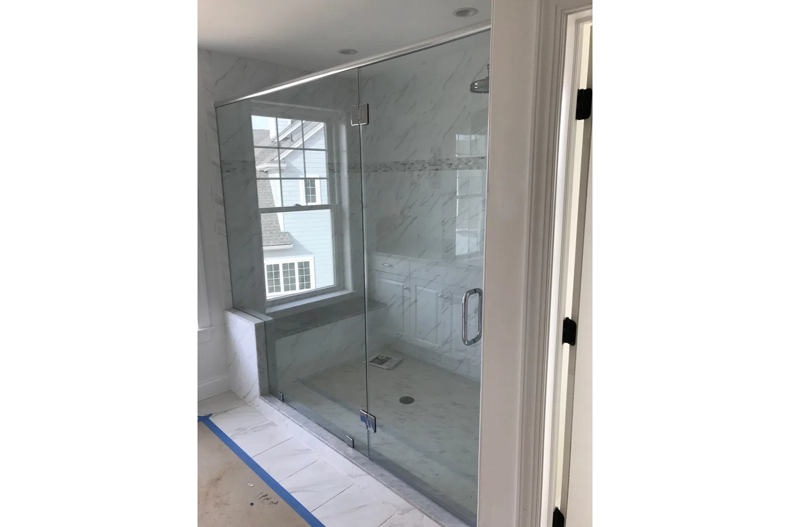 Modern bathroom with a frameless glass shower enclosure and marble-patterned tiles inside and out.