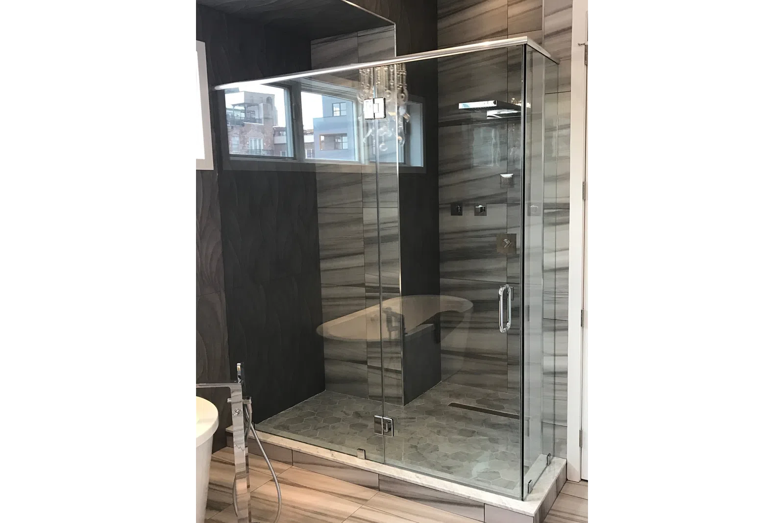 Modern bathroom with glass-enclosed walk-in shower, hexagonal floor tiles, and textured gray wall panels.