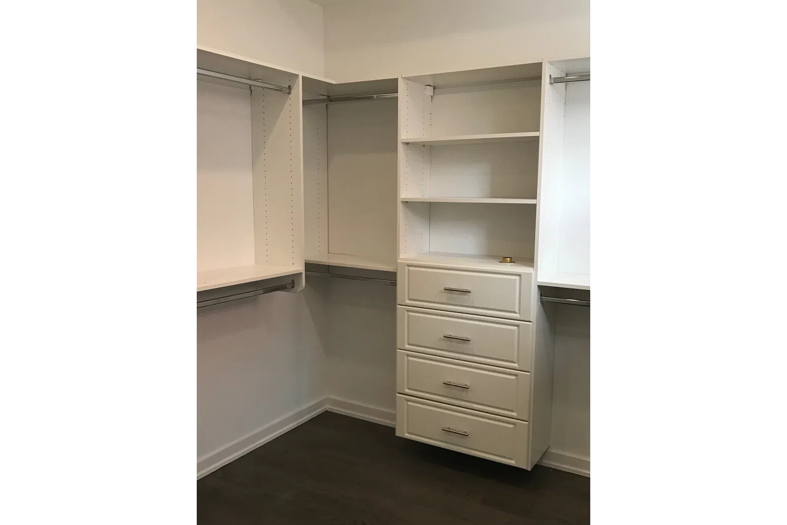 Empty white walk-in closet with built-in shelves, drawers, and hanging rods on dark wood flooring