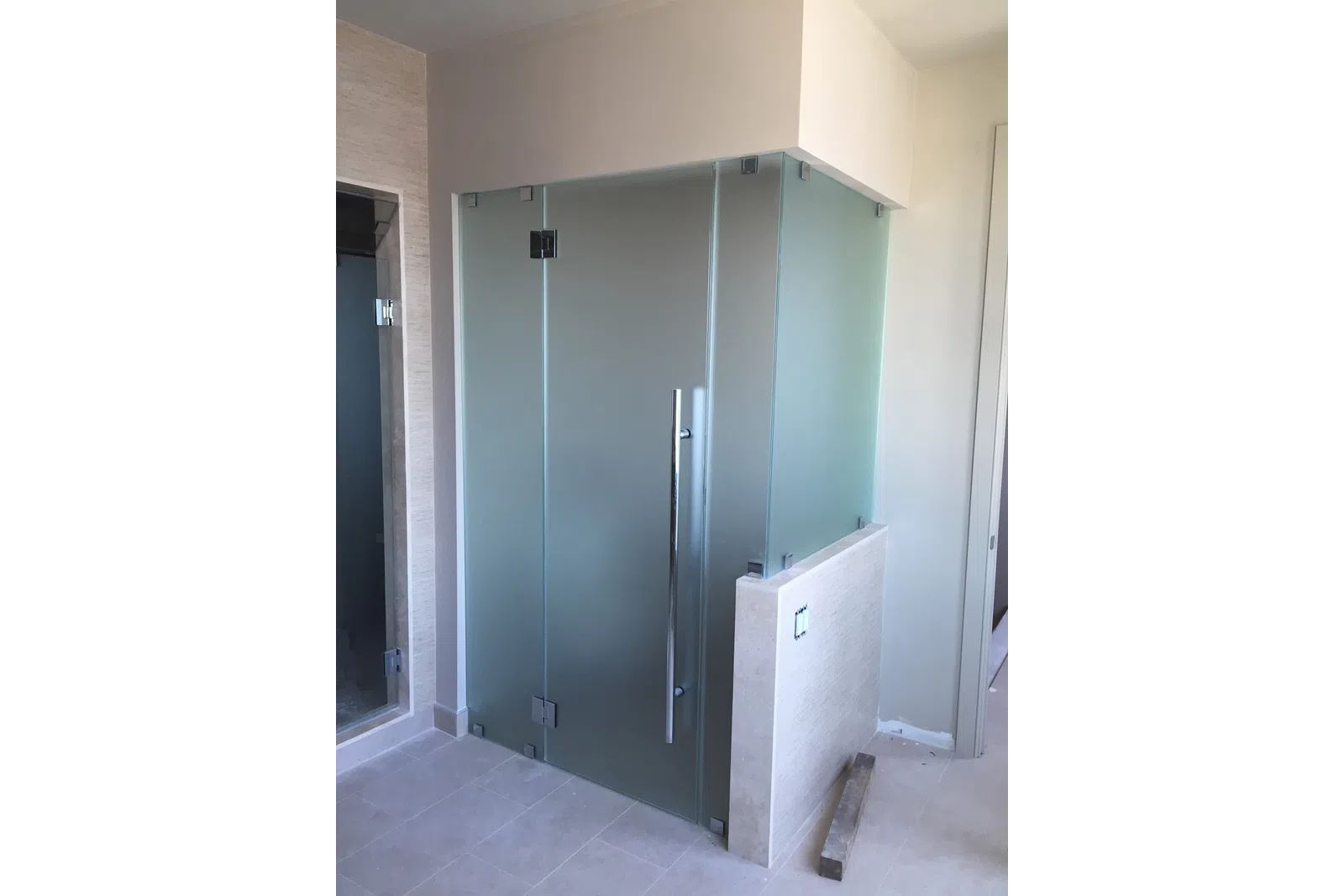 Modern bathroom corner with frosted glass shower enclosure and chrome handle on light tile floor.