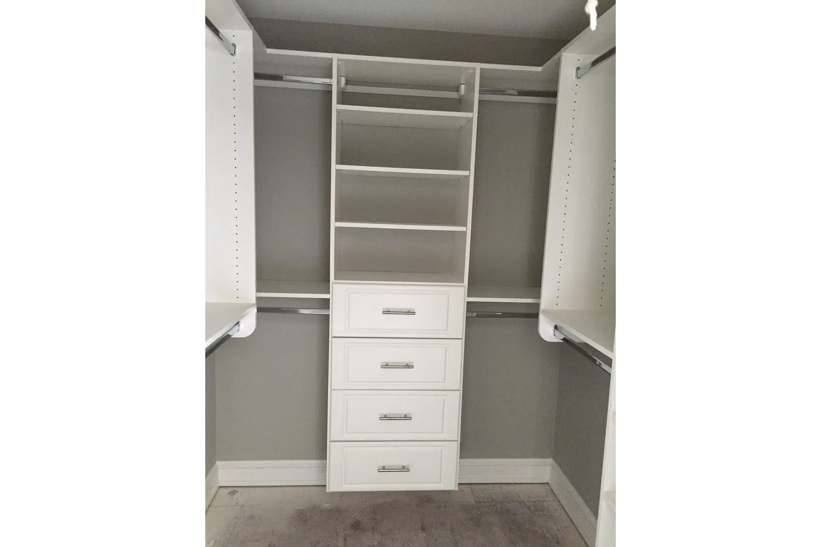 Empty white walk-in closet with built-in shelves, drawers, and hanging rods against gray walls.