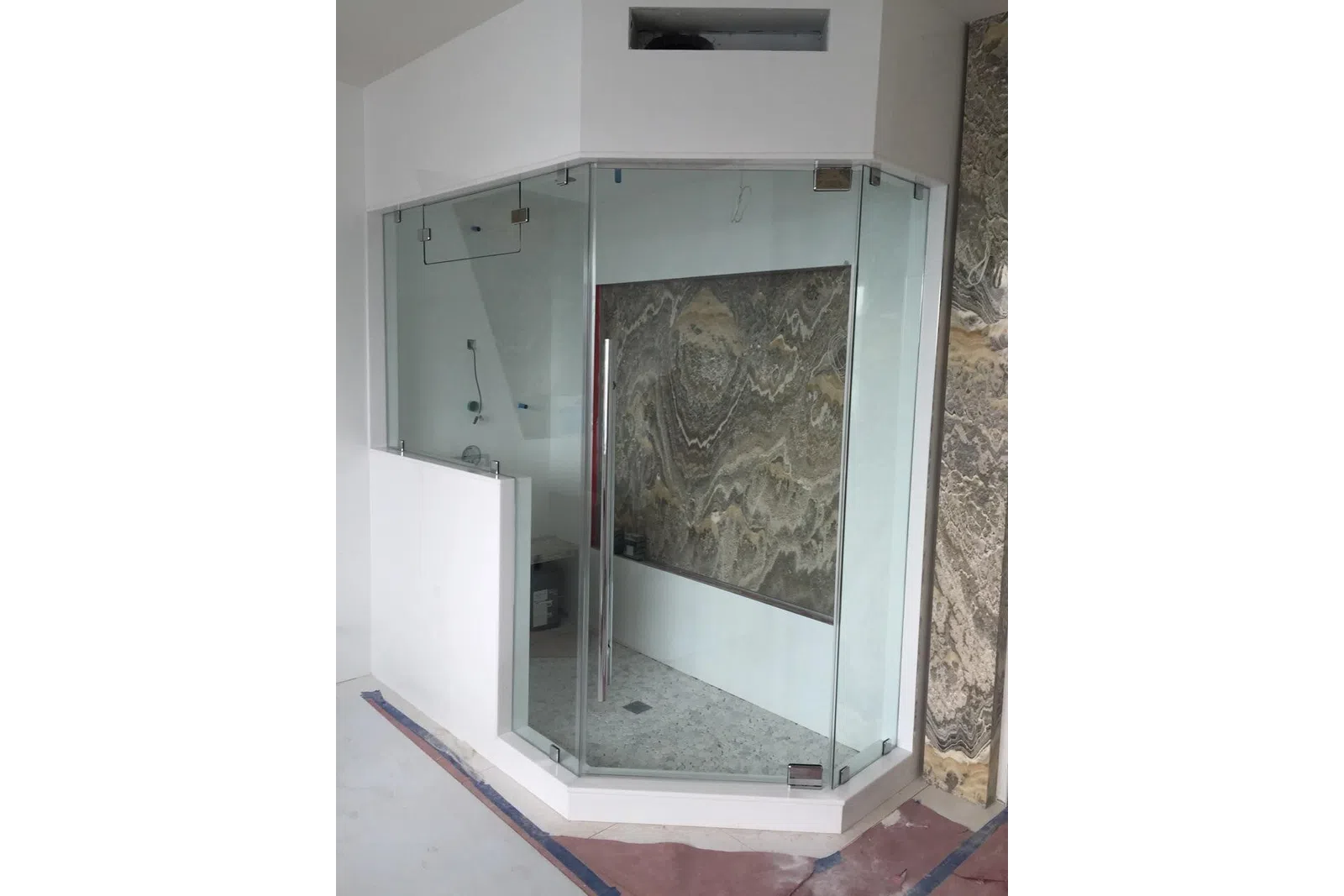 Modern frameless glass shower enclosure with stone tile walls and floor under construction in bathroom.