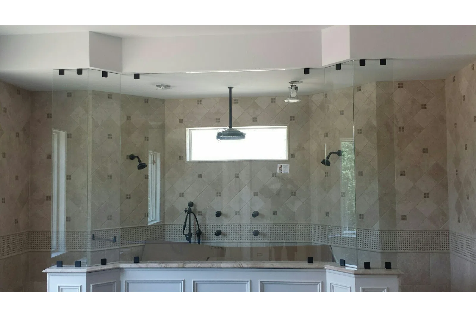Modern bathroom with large frameless glass shower enclosure, multiple showerheads, and beige tiled walls.