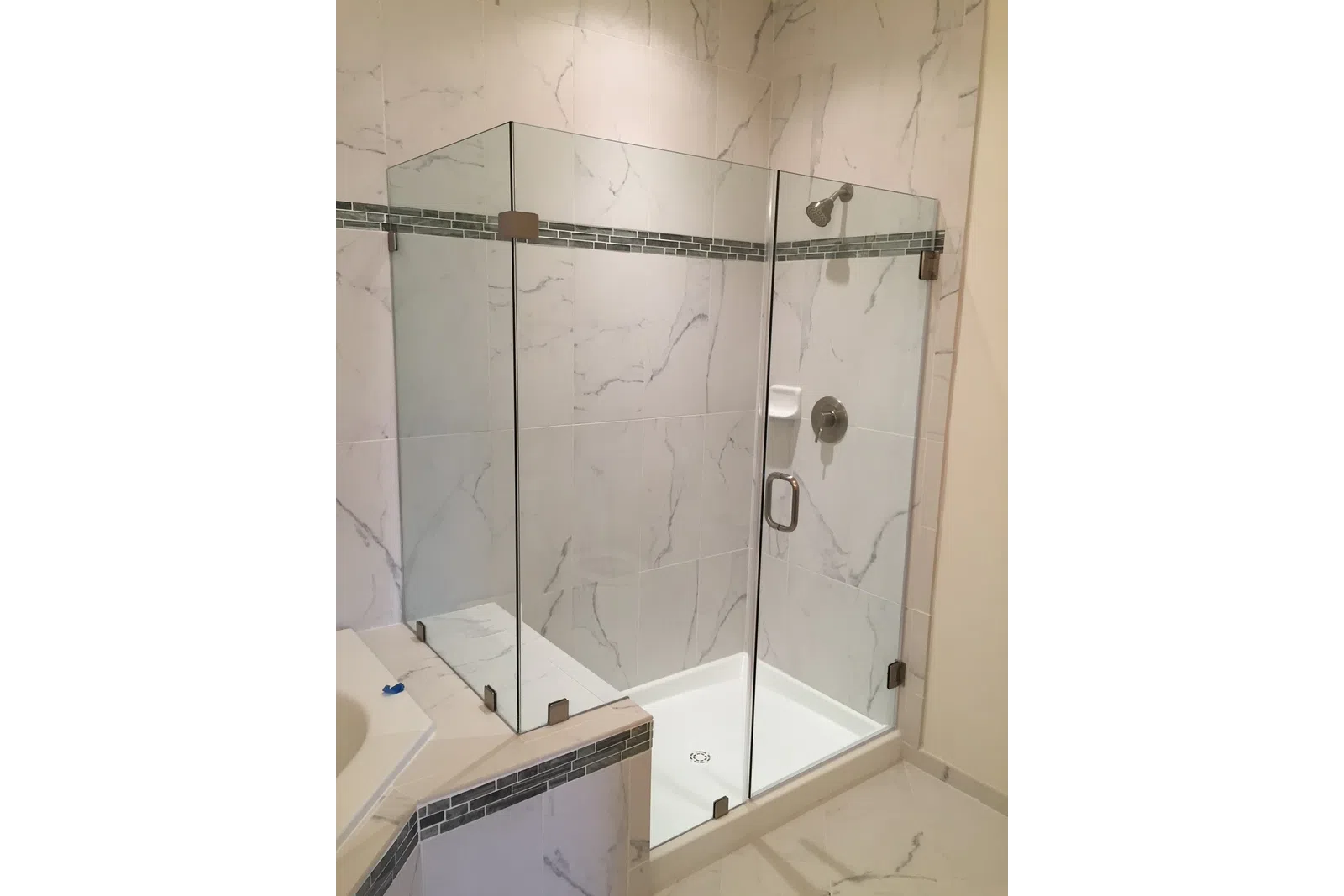 Modern walk-in glass shower with marble tile walls and black mosaic trim in a bathroom corner.