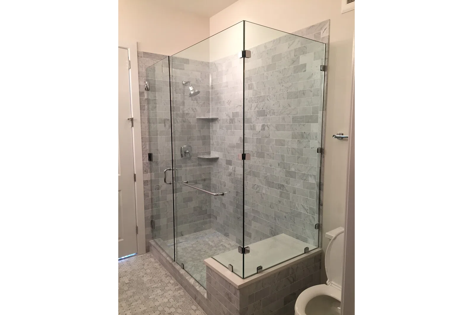 Modern bathroom with glass-enclosed shower, gray mosaic tiles, and stainless steel fixtures including showerhead and grab bar