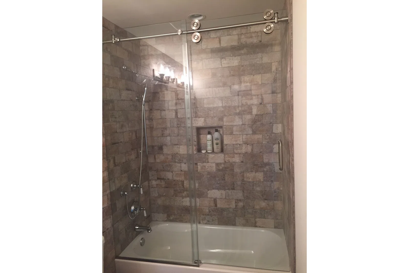 Modern bathroom with a bathtub, stone tile walls, glass sliding shower doors, and built-in shampoo niche.