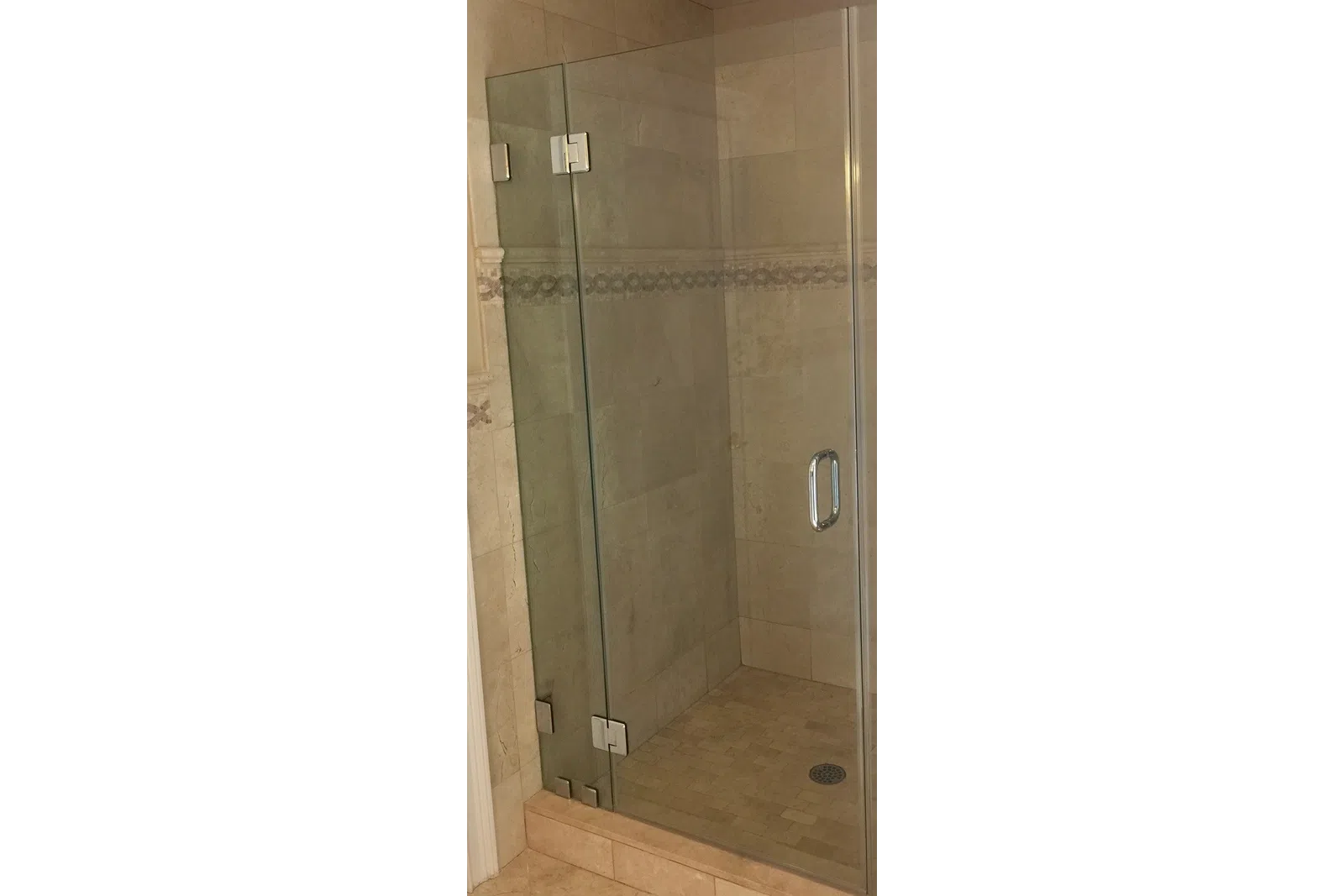 Modern walk-in shower with glass door and beige tiled walls and floor with decorative border