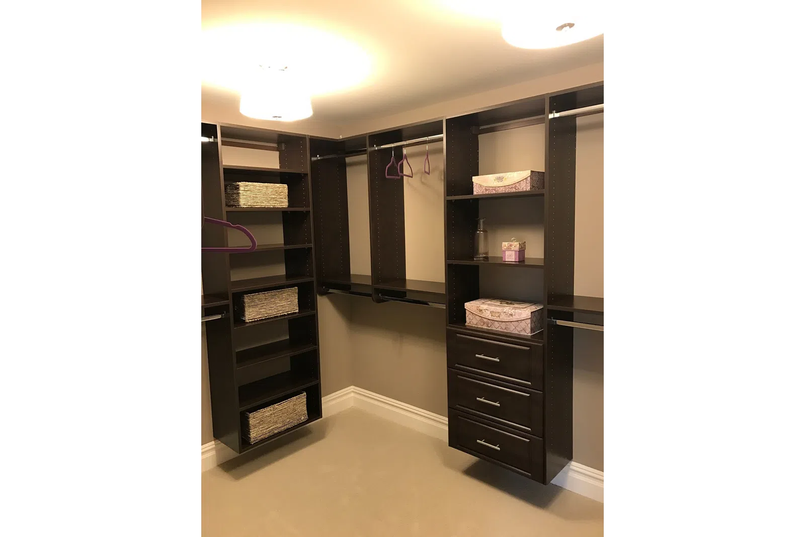 Spacious walk-in closet with dark wood shelves, drawers, hanging rods, baskets, and decorative boxes