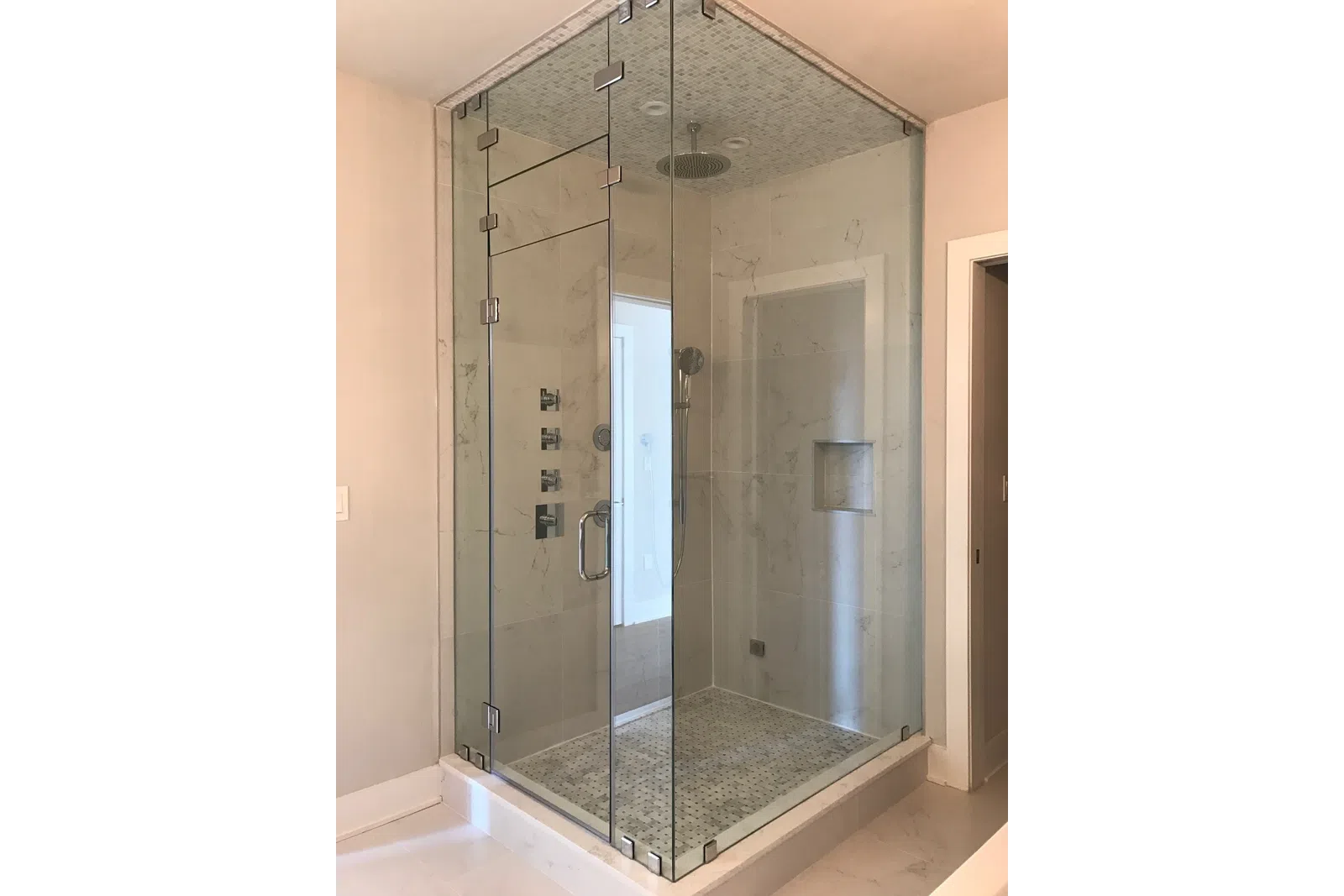 Modern frameless glass shower enclosure with marble tile walls and rain showerhead in a bathroom