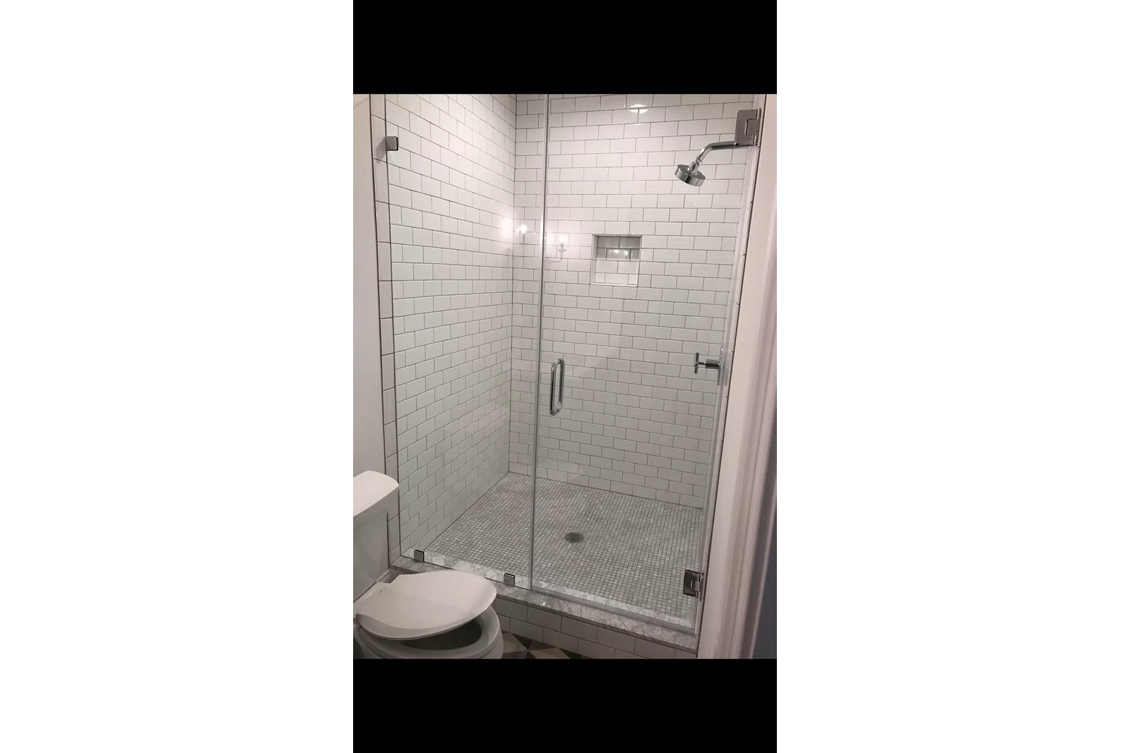 Modern bathroom with glass shower enclosure, white subway tiles, and a toilet with an open lid.