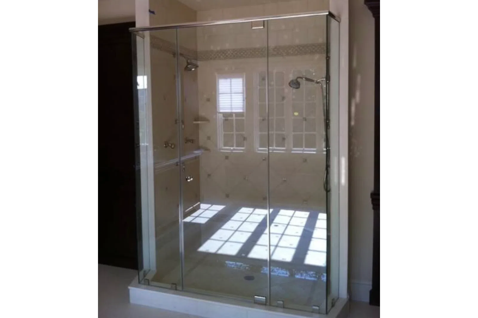 Modern glass shower enclosure with chrome fixtures and sunlight reflection inside bathroom.