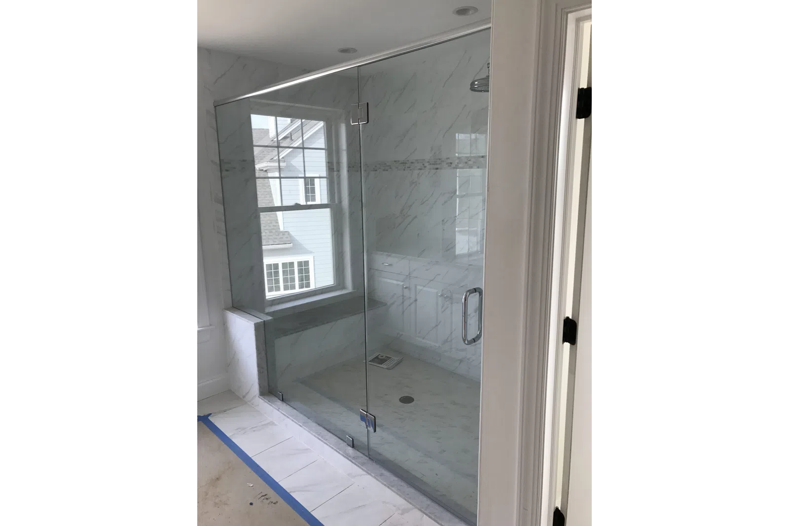 Modern walk-in shower with glass enclosure, marble tile walls and floor, and built-in bench under window.