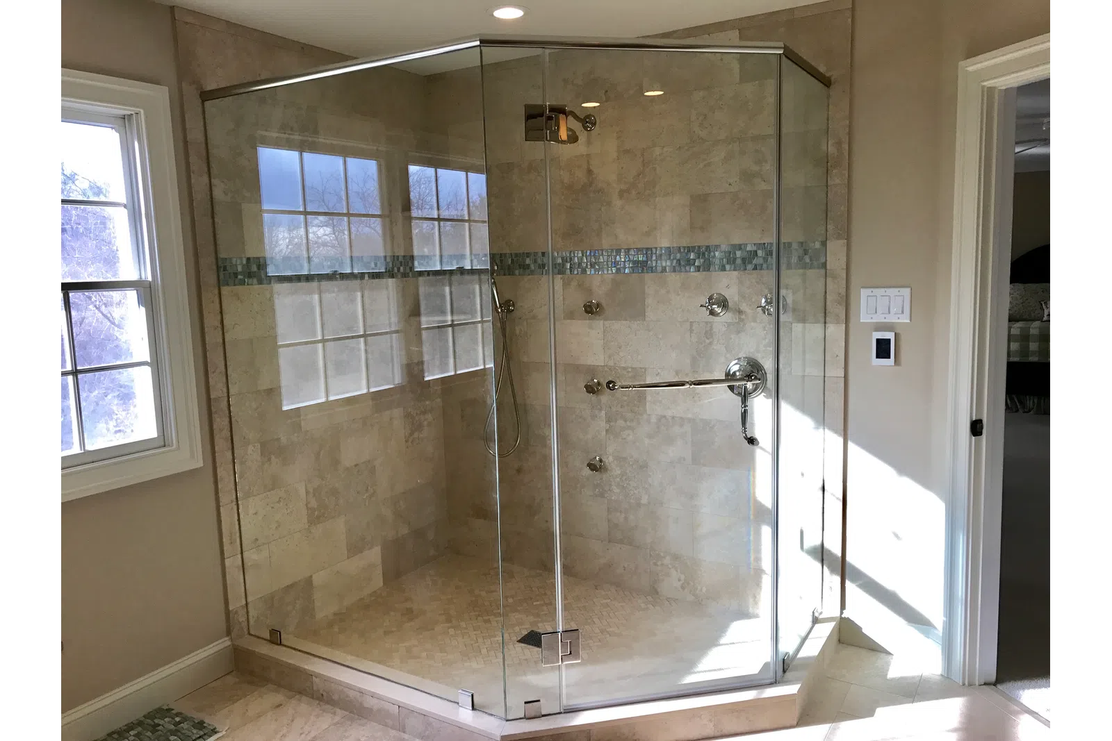 Modern frameless glass shower enclosure with beige tile walls and decorative blue tile border