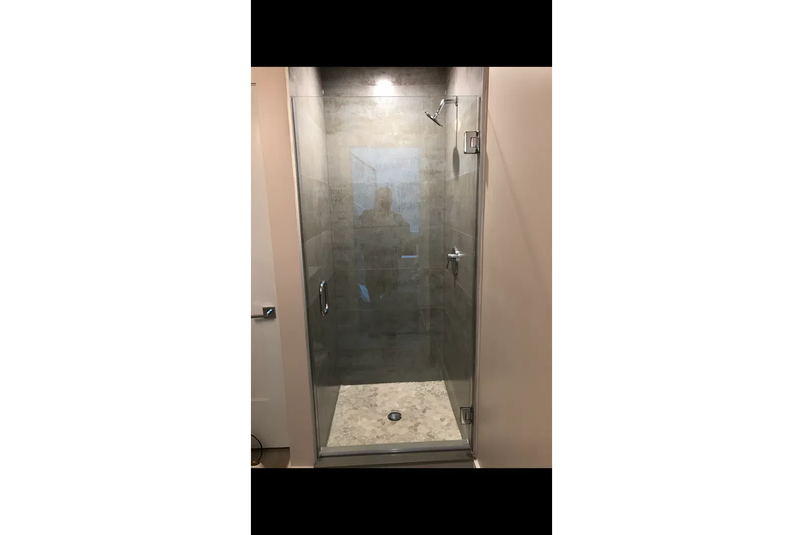 Modern walk-in glass shower with gray stone tiles and pebble floor in a minimalist bathroom design.