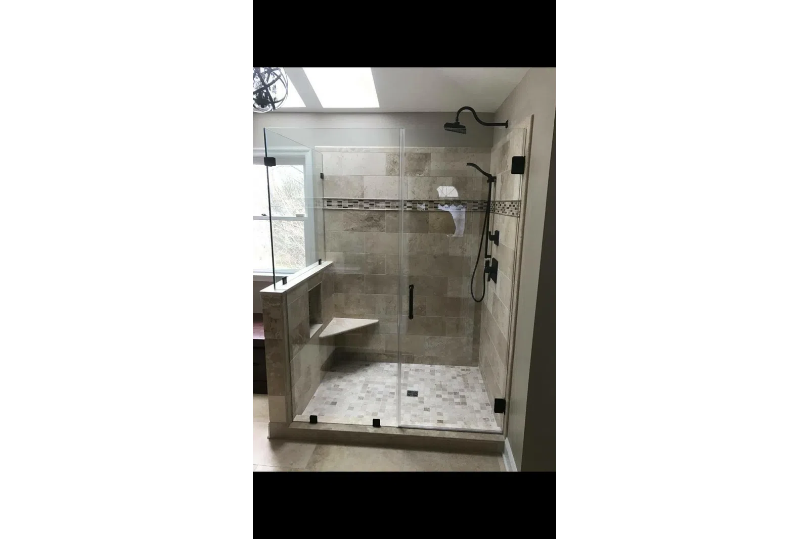 Glass-enclosed walk-in shower with beige tiles, mosaic accent strip, built-in bench, and black fixtures.