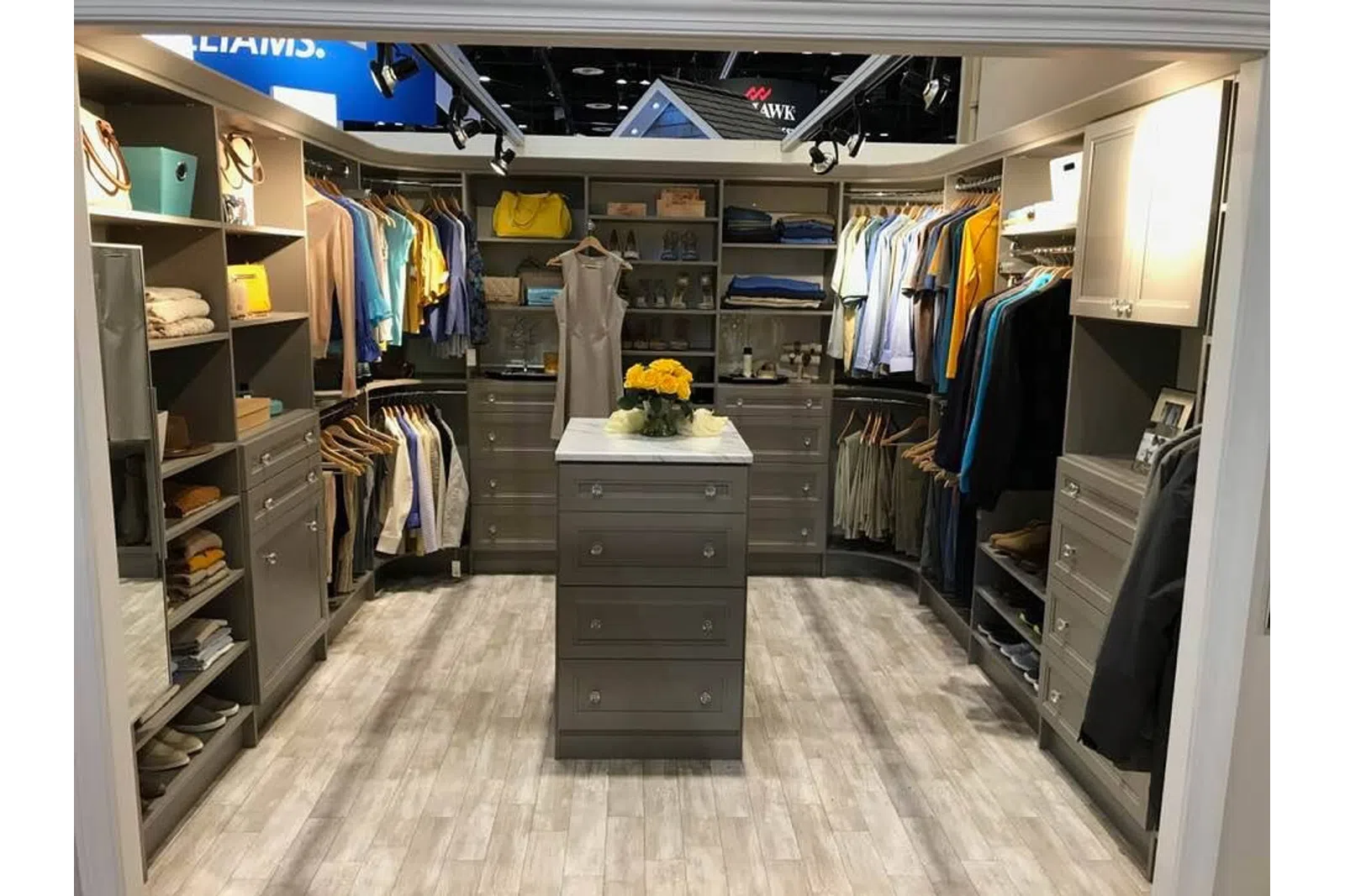 Modern walk-in closet with gray cabinetry, organized clothes, and central island with flowers on top