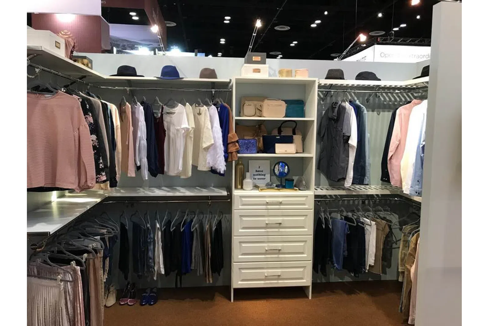 Organized walk-in closet with hanging clothes, shelves with bags and hats, and drawers in the center.