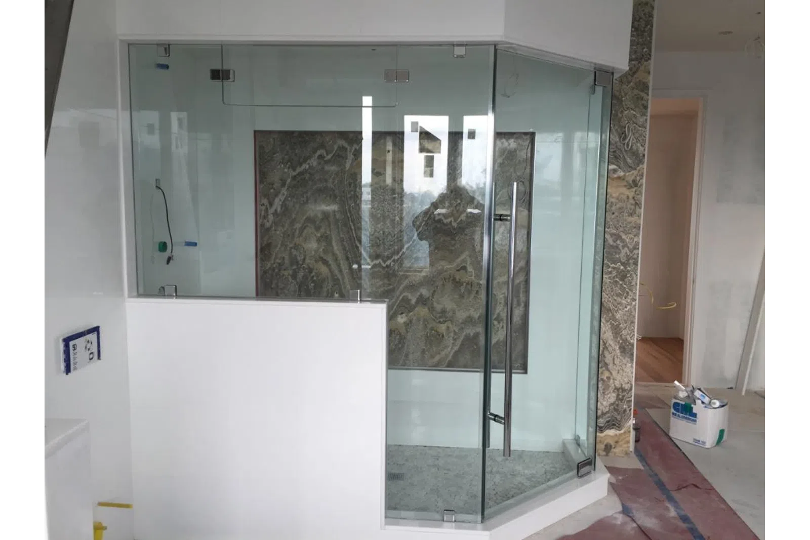 Modern glass shower enclosure with marble wall panels in a bathroom under construction.