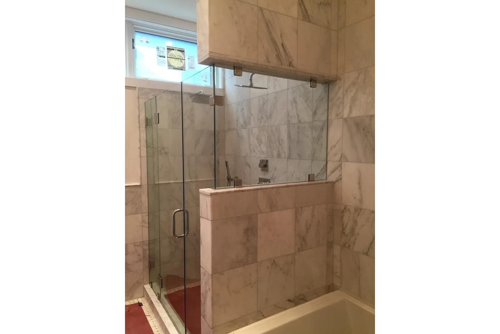 Modern bathroom with marble tile walls and glass shower enclosure featuring a rain showerhead.