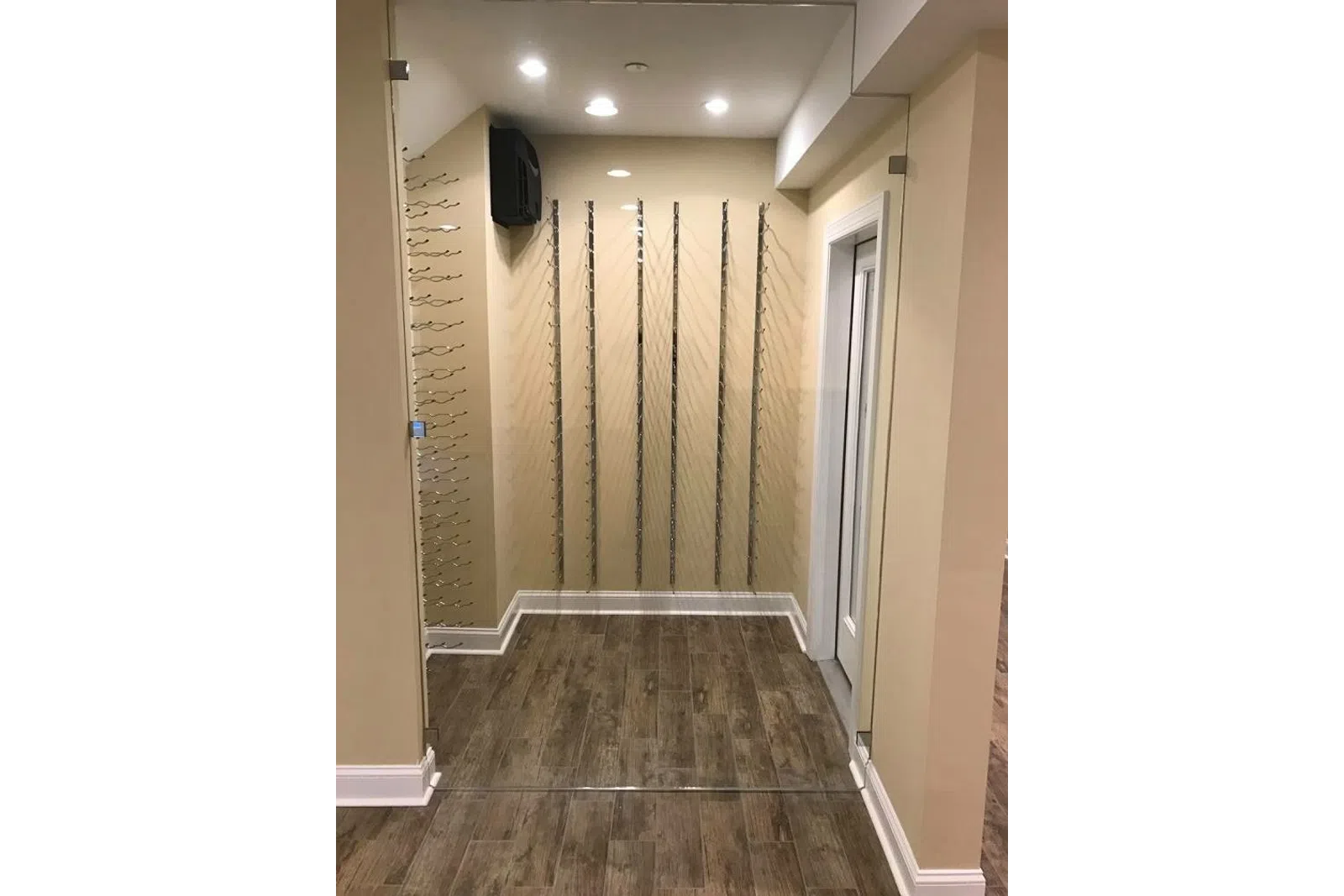 Empty wine glass rack installation in small room with wooden floor and beige walls under recessed ceiling lights