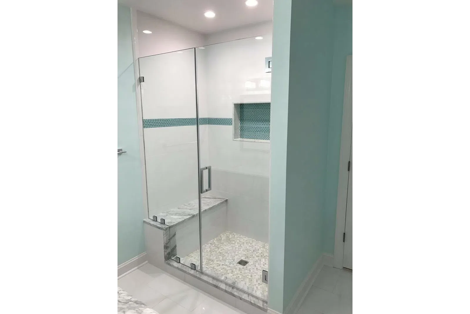 Modern bathroom shower with glass door, built-in bench, mosaic floor tiles, and blue tiled accent strip.